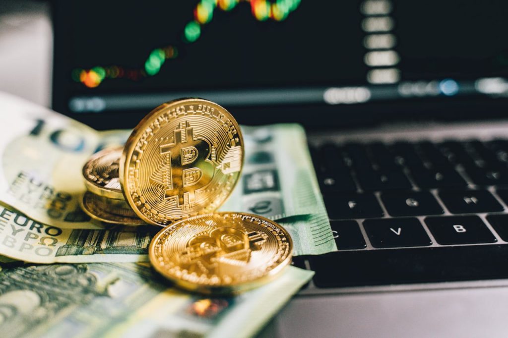 Bitcoin coins and Euro banknotes on a laptop with stock graph in background.